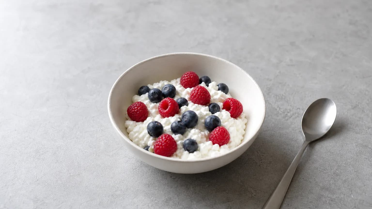 Small bowl of cottage cheese topped with a few berries on matte grey stone