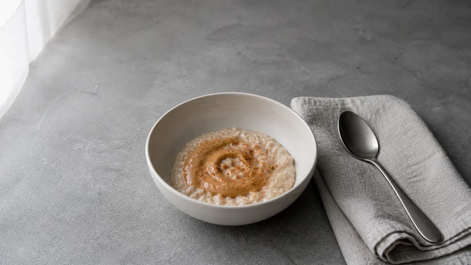 Small bowl of soft oatmeal with a light peanut butter swirl on matte grey stone
